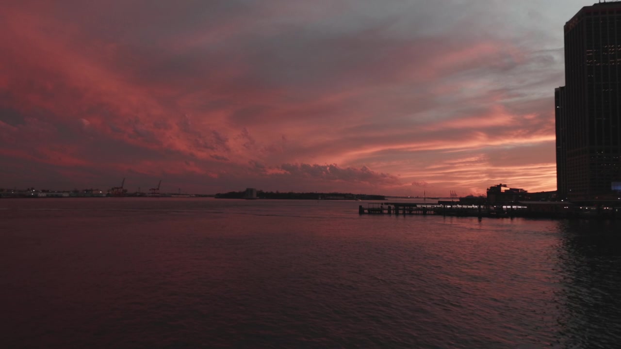 A dramatic red sunset casts vivid hues over a waterfront, with a silhouetted cityscape on the right. Ideal for use in travel and urban lifestyle content.