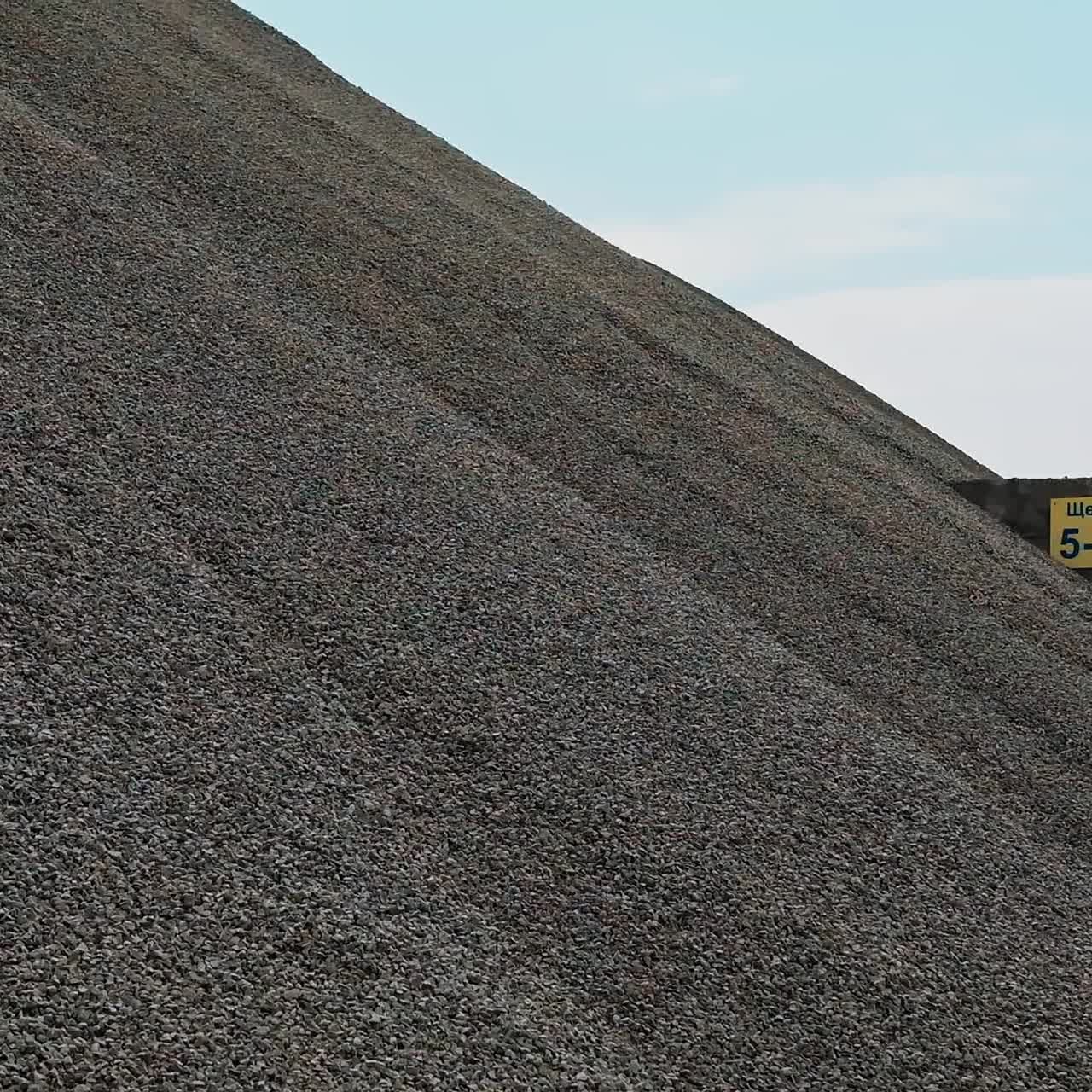 Large pile of gravel. Building materials in the concrete plant outdoors. Gravel production. Crushed stones on a big heap against the clear sky.