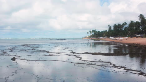 Aerial-view-of-Praia-do-Forte-beach,-the-coral-reef,-palm-tree-area-and-the-clouds-reflecting-on-the-ocean,-Praia-do-Forte,-Bahia,-Brazil