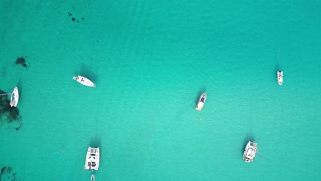 boats floating at turquoise blue sea at la pelosa, sardinia, italy - aerial 4k birdseye