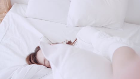 mujer asiática con camisa blanca hablando con una videollamada selfie caminando hasta la cama con una sonrisa