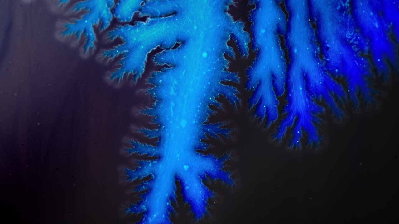 Intricate, macro shot of blue ink spreading on a dark surface with vivid patterns