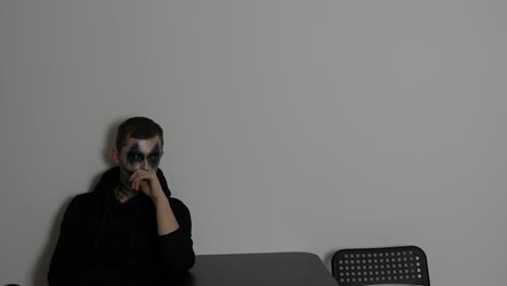 hombre solo sentado con el maquillaje de payaso oscuro al lado de la mesa