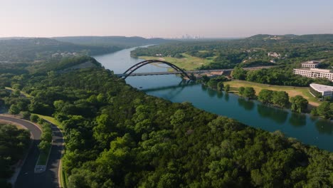 aerial sweep of the iconic pennybacker 360 bridge in austin, texas during hazy summer sunrise morning with downtown skyline in backdrop