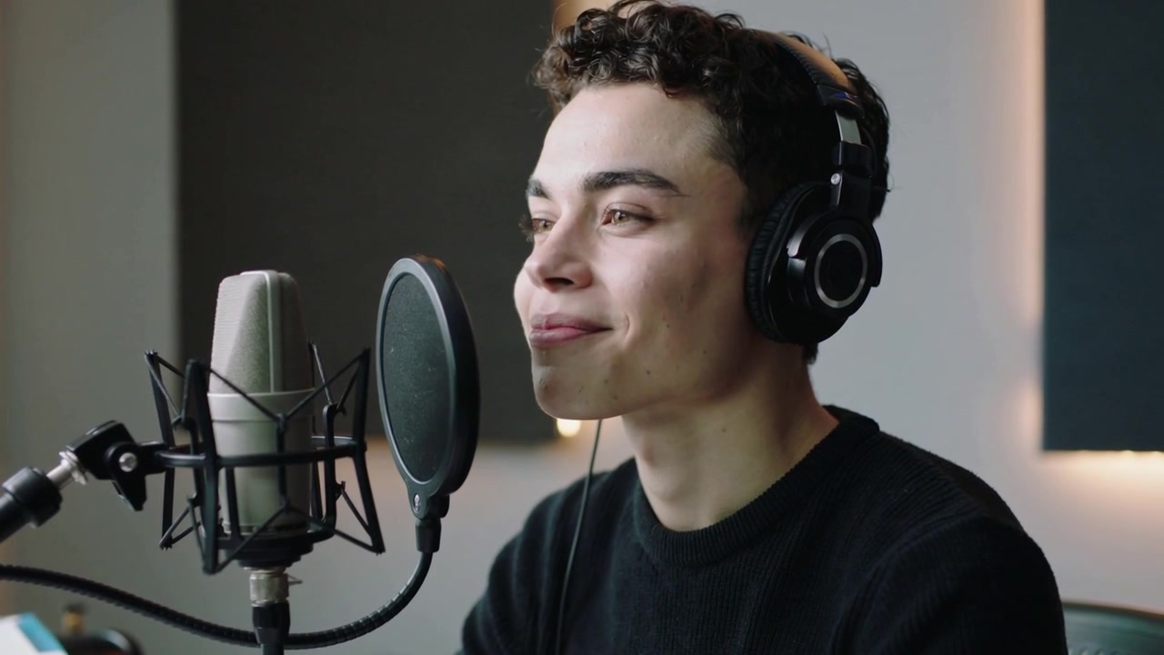 Starting male vocalist performing warmup at studio with cond mic, pop-filter, headphones, crewneck
