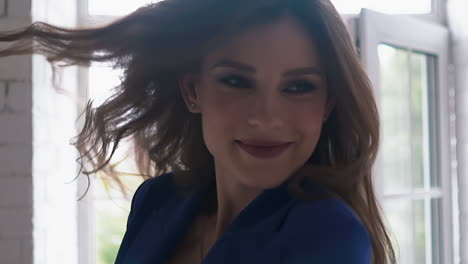 una mujer bonita gira sacudiendo el pelo largo castaño cerca de la ventana