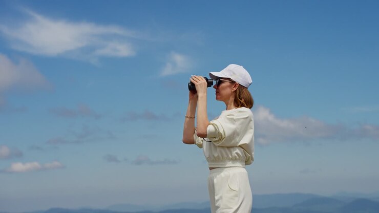 Donna con binocolo in cima a una montagna