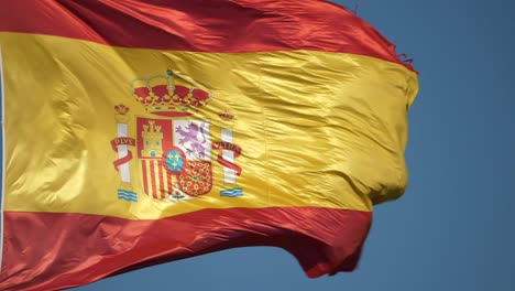 Closeup-of-Spanish-flag-against-blue-sky-background,-static,-windy-day