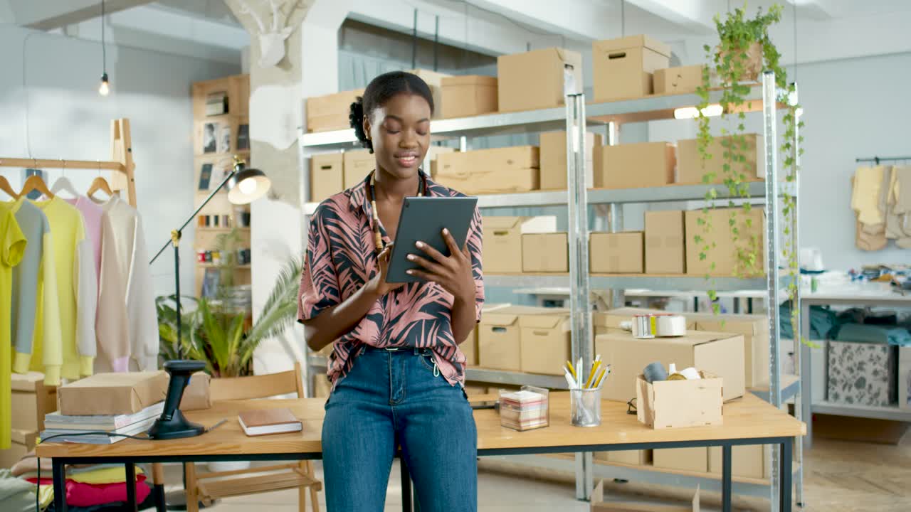African American designer woman usign a tablet leaning on the table in a fashion clothing store