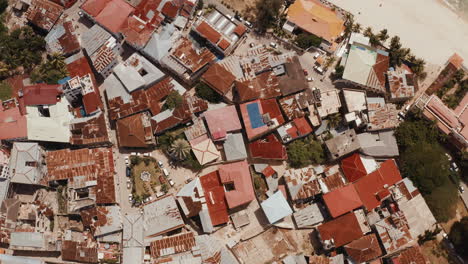 Bird's-eye-view-of-Stone-Town-buildings-roofs,-coastline,-beach,-and-anchored-fishing-boats-on-a-sunny-day