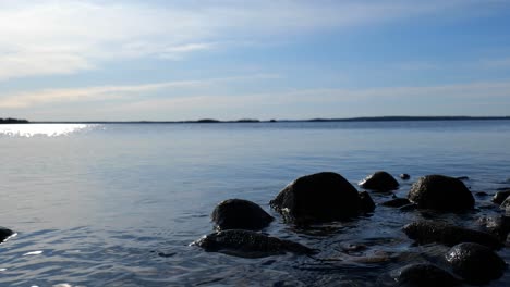 Relajante-Paisaje-Lacustre-Con-Agua-Ondeando-Suavemente-Hacia-Las-Rocas-En-La-Costa