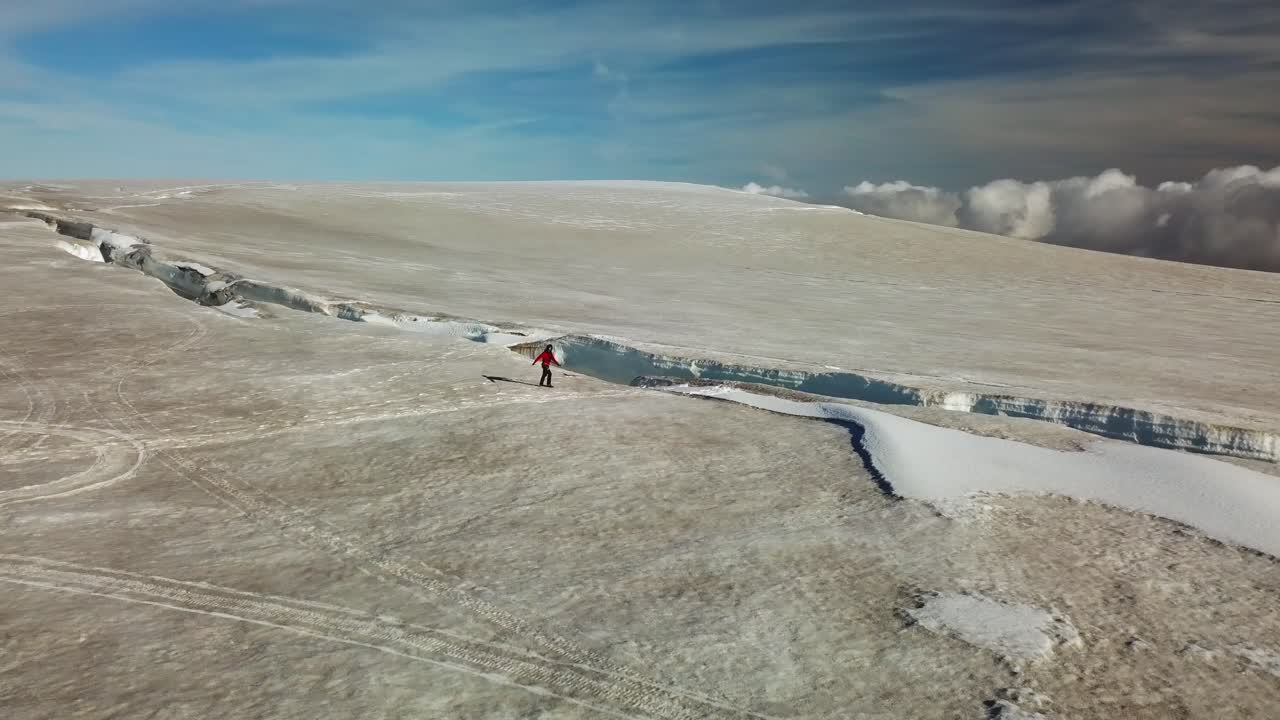 vista aérea de un escalador caminando hacia el borde de una grieta de hielo, agrietada en la superficie del hielo de un glaciar islandés