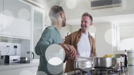 Animation-of-light-spots-over-diverse-male-couple-cooking-dinner-in-kitchen