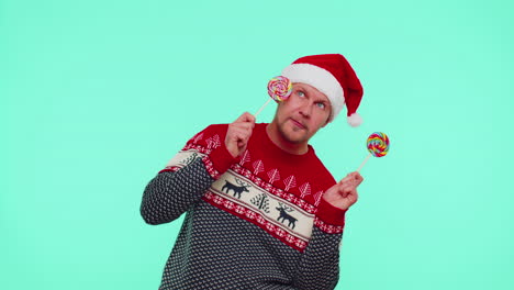 Funny-man-in-red-New-Year-sweater,-hat-holding-candy-striped-lollipops,-dancing,-making-silly-faces