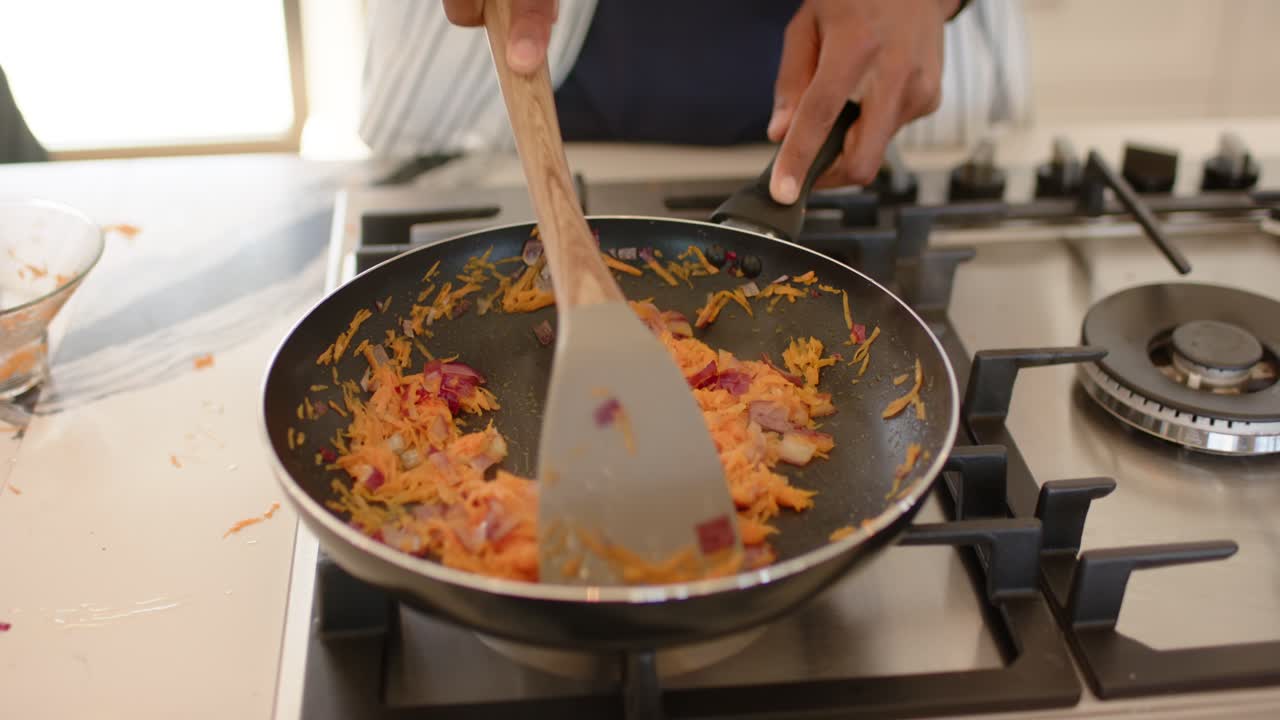 Homem ouvindo o som de algo fritando no fogão da cozinha, usando uma espátula para mexer cenouras e cebolas uniformemente na panela