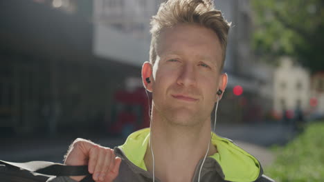 portrait of confident young man looking at camera wearing earphones listening to music enjoying healthy urban lifestyle in city street background