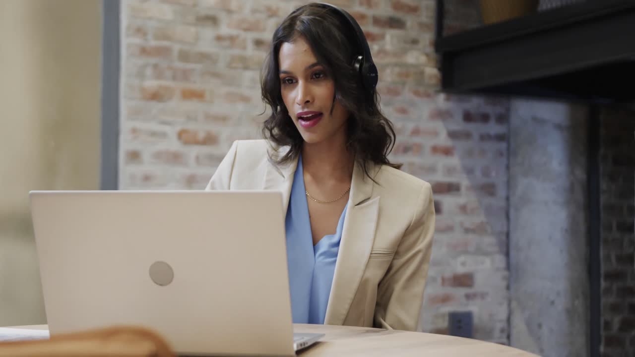Donna d'affari casual birazziale che effettua una videochiamata usando un laptop nell'area lounge dell'ufficio, al rallentatore.