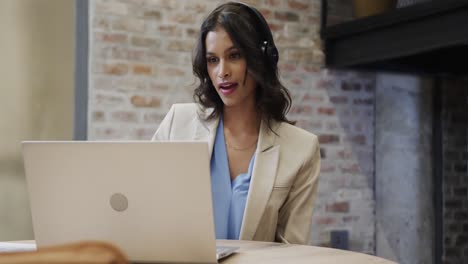 mujer de negocios casual biracial haciendo una videollamada usando una computadora portátil en el salón de la oficina, cámara lenta