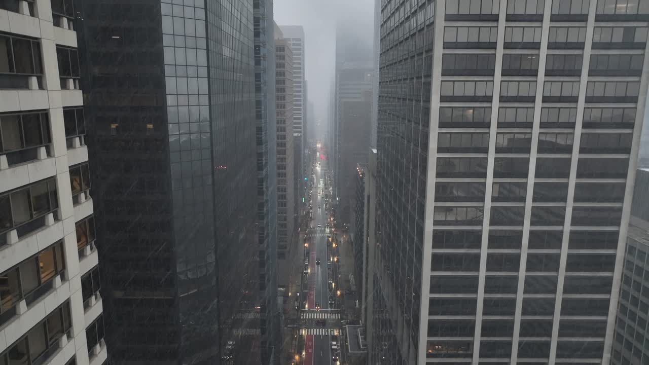 Veduta aerea cinematografica di una città americana del centro durante una nevicata e pioggia, con semafori che brillano tra alti grattacieli negli USA. Atmosfera cupa e malinconica da film noir. Carrellata verso l'alto