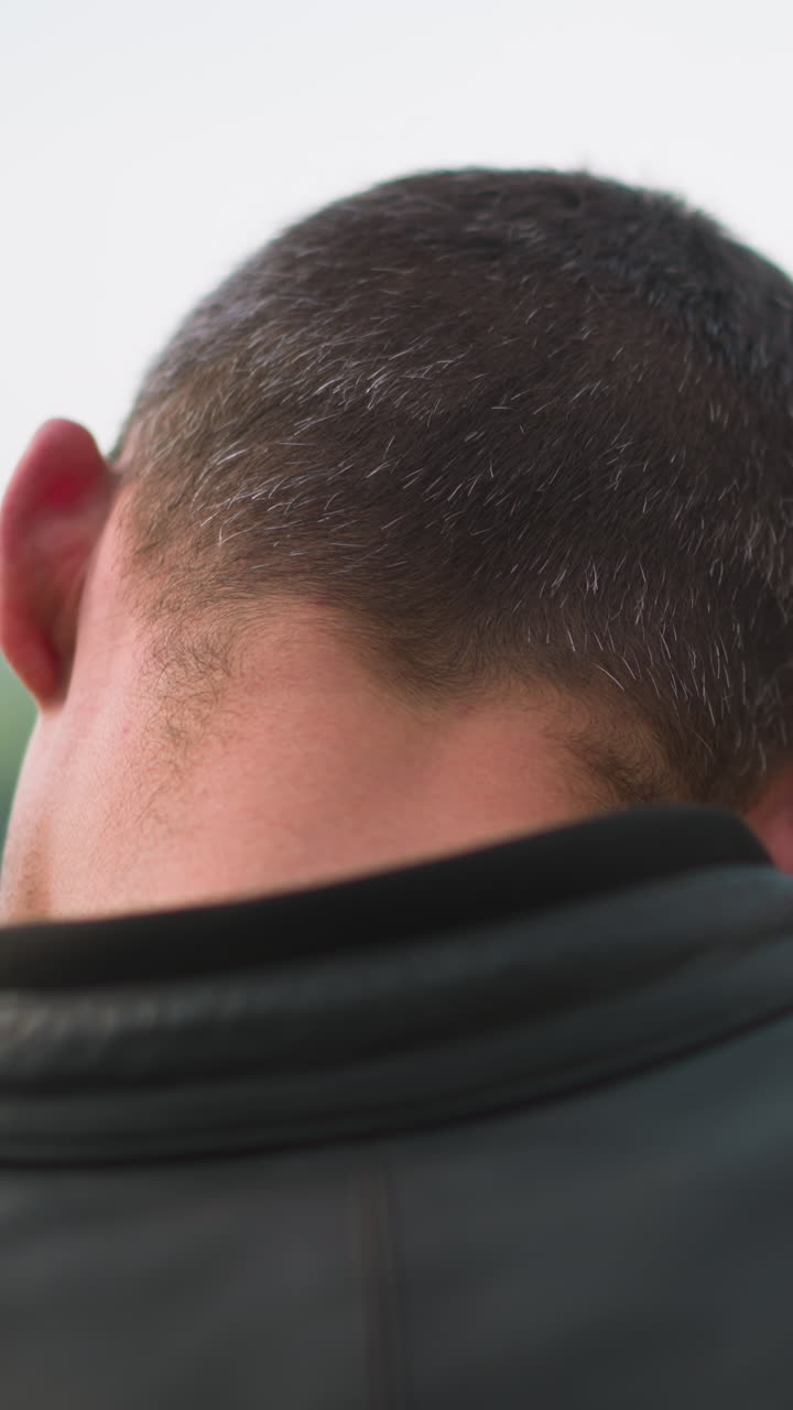 Guy in black leather clothes hugs long fair haired lady standing against picturesque lake on summer day close backside view slow motion