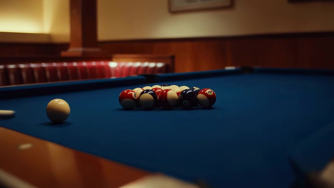 Pool balls scatter across blue felt surface after cue impact, showing motion from clustered arrangement to wide spread pattern under warm indoor lighting with focused view of table area.
