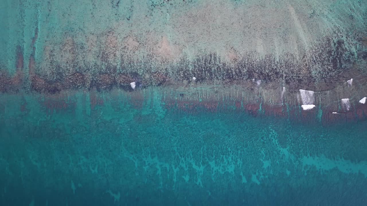 Abstract top-down aerial view of the Mauritius coastline and fringing coral reef. Vibrant turquoise shallows meet the deep blue ocean, highlighting natural patterns and wave breaks