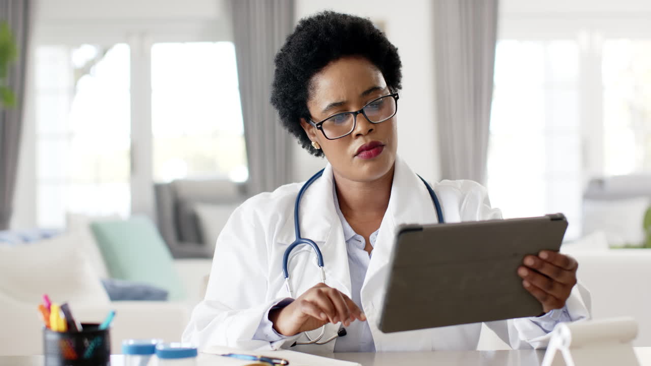 African American female doctor in a white lab coat reviews a tablet on video call consultation