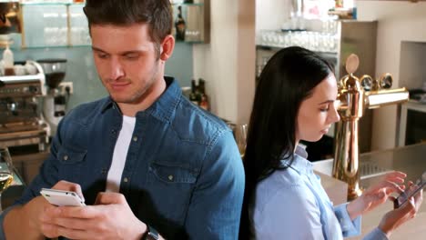 couple standing back to back while using laptop
