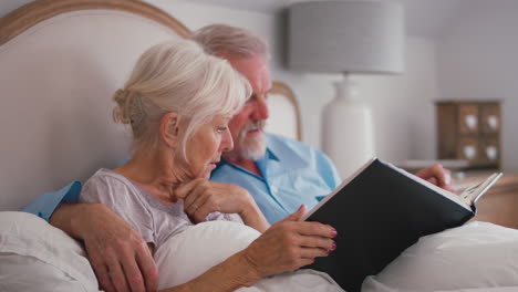 Pareja-De-Ancianos-Jubilados-En-La-Cama-En-Casa-Mirando-Juntos-El-álbum-De-Fotos