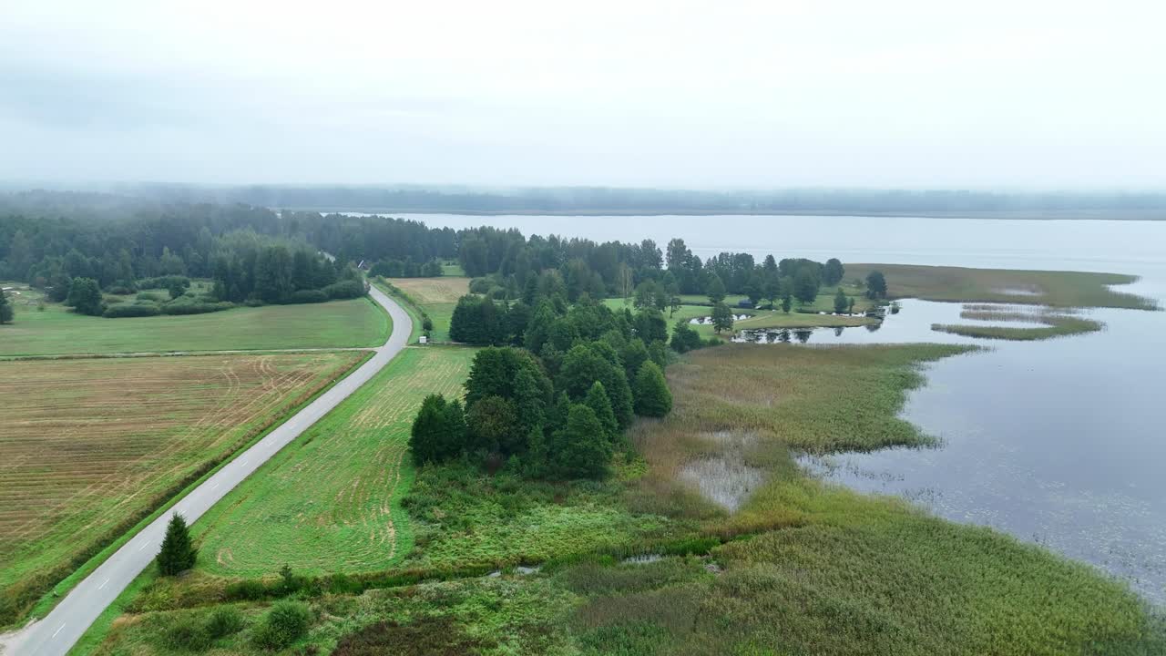 Country road alongside Usma lake in Latvia during misty morning, aerial shot