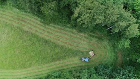 Top-down-aerial-of-a-tractor-mowing-a-field-in-a-narrow-corner-surrounded-by-trees