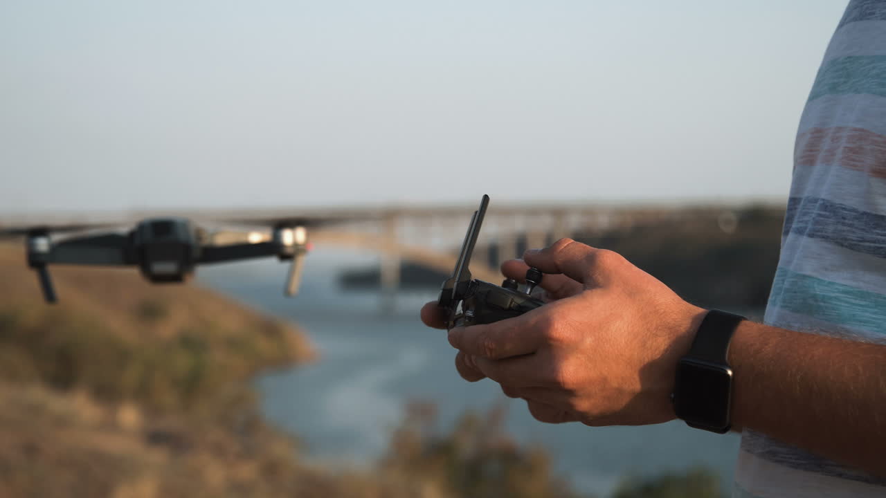 Drone Pilot Controlling Drone Over River and Bridge
