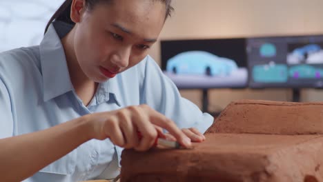 close up of asian woman automotive designer works on the sculpture of car clay using knife to smooth out the surface and create details in the design in the studio