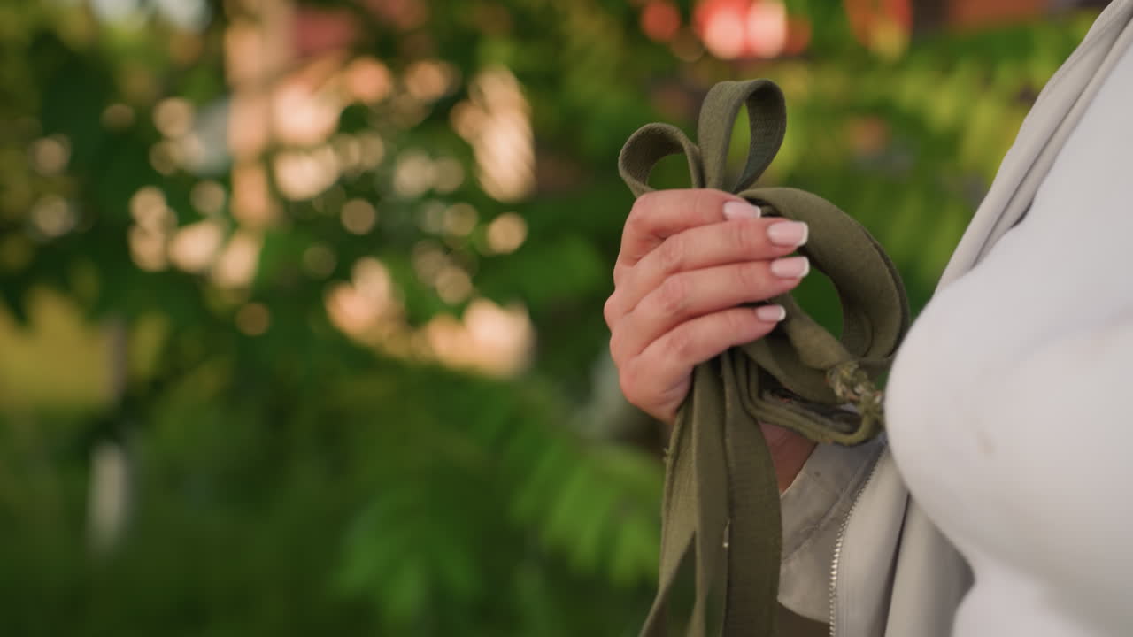 야외에서 산책하는 동안 녹색 로프를 들고 있는 손의 클로즈업, 자연 환경에 둘러싸여, 배경에 흐릿한 초록색과 잎을 통해 필터링되는 빛