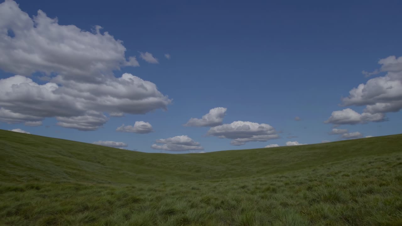Wide-angle video shot of a serene landscape with rolling green hills under a vast blue sky dotted