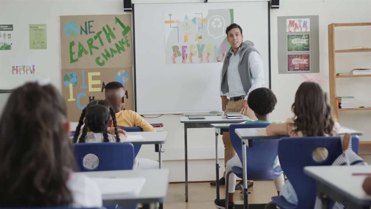 un maestro masculino diverso hablando y niños en los escritorios en la clase de la escuela primaria, cámara lenta