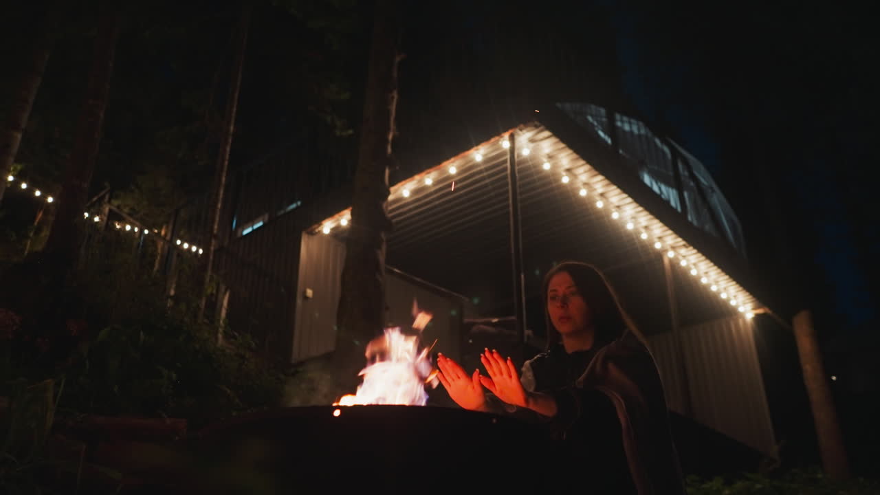 한 여인이 꽃불 근처에 서서 손을 따뜻하게 하고 있다. 부인은 편안한 담요로 인 채 멋진 집 안에 서서 저녁의 추위를 막으려고 노력한다.