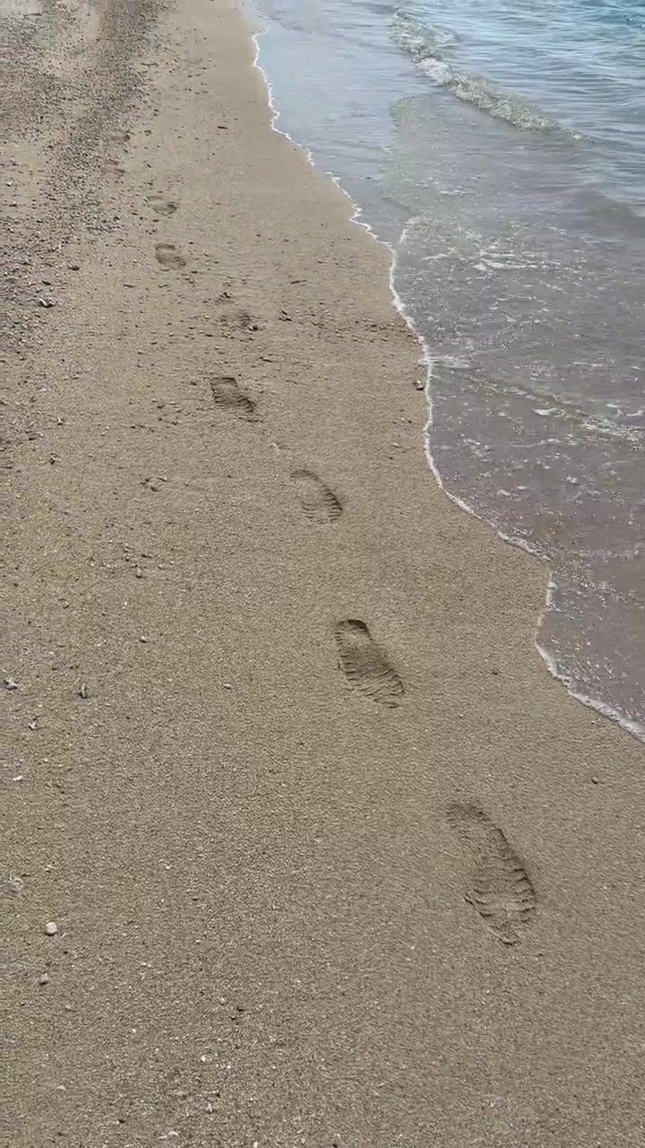 Onde dell'oceano che cancellano le impronte su una spiaggia sabbiosa