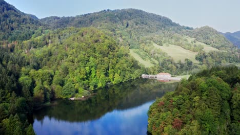 presa en el borde de un lago azul profundo que refleja en el paisaje montañoso y los bosques circundantes, drone aéreo suave