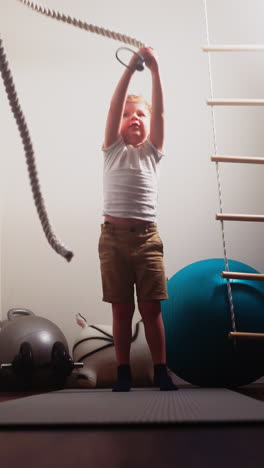 little boy hits battle rope on floor standing near professional gym equipment. active child enjoys exercise for pumping up body muscles slow motion