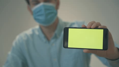 businessman with face mask holding a green screen smartphone