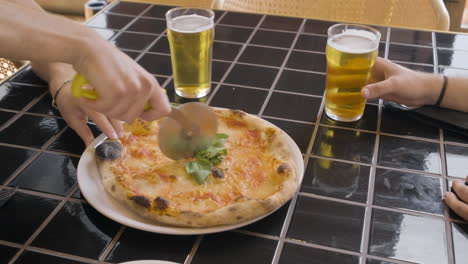 top view of a diner's hand cutting pizza at a restaurant table