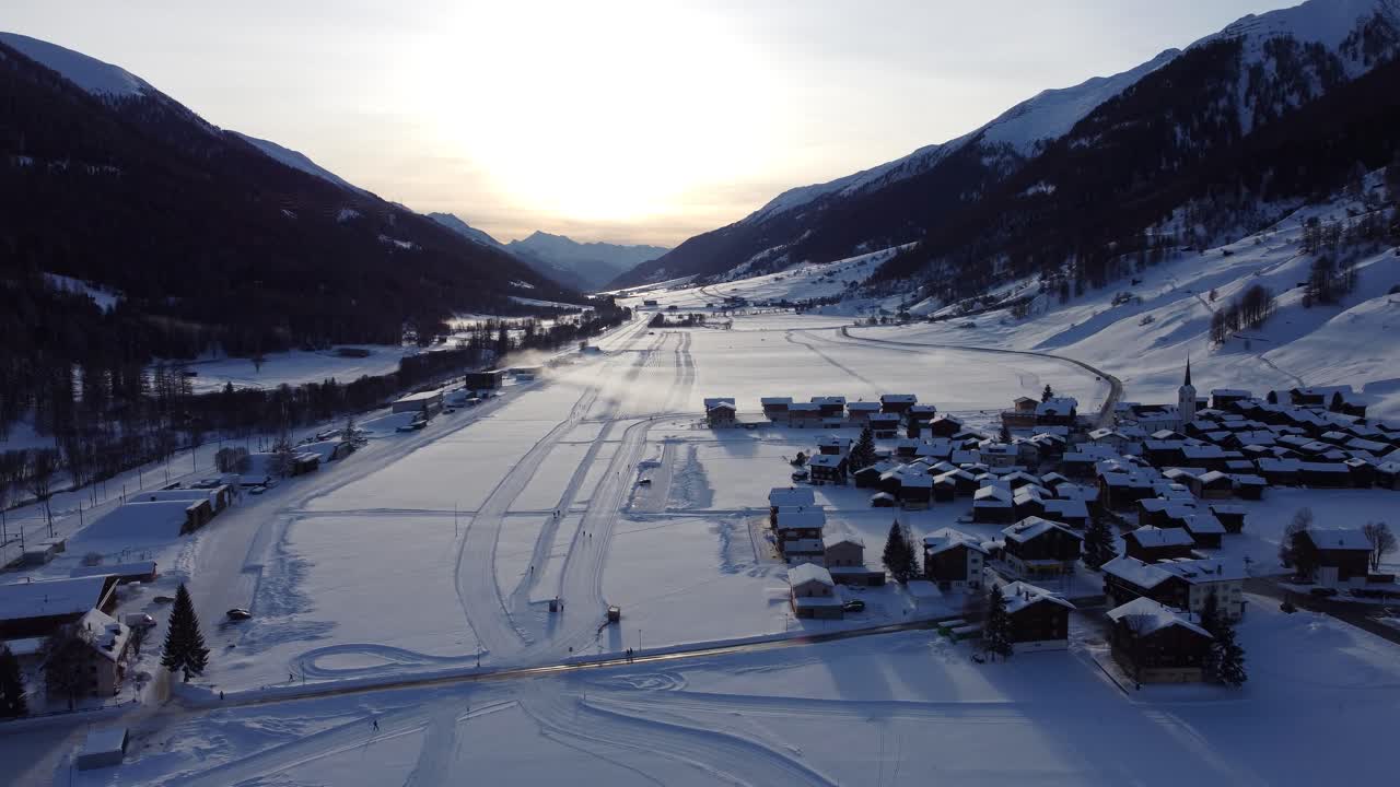 Letecké záběry zasněžených alpských vesnic v Obergoms, Švýcarsko, s horami Furka Pass, které dominují zimní krajině. Tradiční města obklopená hlubokým alpským sněhem.