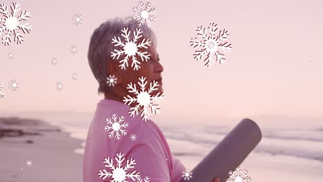 Animation-of-christmas-snow-falling-over-senior-biracial-woman-on-beach