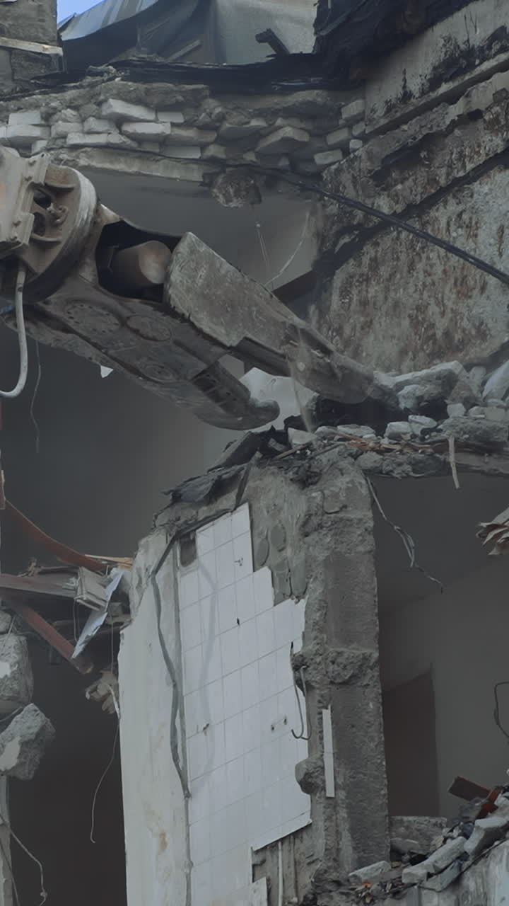 Breaking concrete walls and floors with the help of machinery. Dusty area of destruction site. Powerful claw ruins the house. View from below. Vertical video