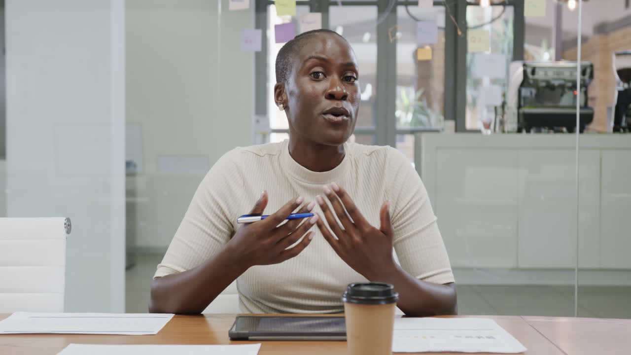 retrato de una mujer de negocios afroamericana con la cabeza afeitada haciendo una llamada de video en la oficina, en cámara lenta