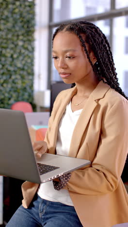Vertical video of african american casual businesswoman using laptop in office, slow motion