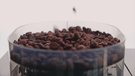 brown roasted coffee beans dropping into container for grinding