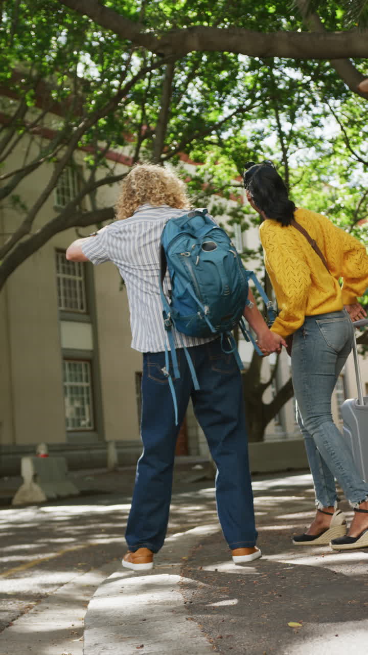 Vertical video of happy diverse couple hailing taxi with luggage in city