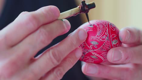 cerca del artista dibujando diseños ornamentados tradicionales en un huevo de pascua rojo